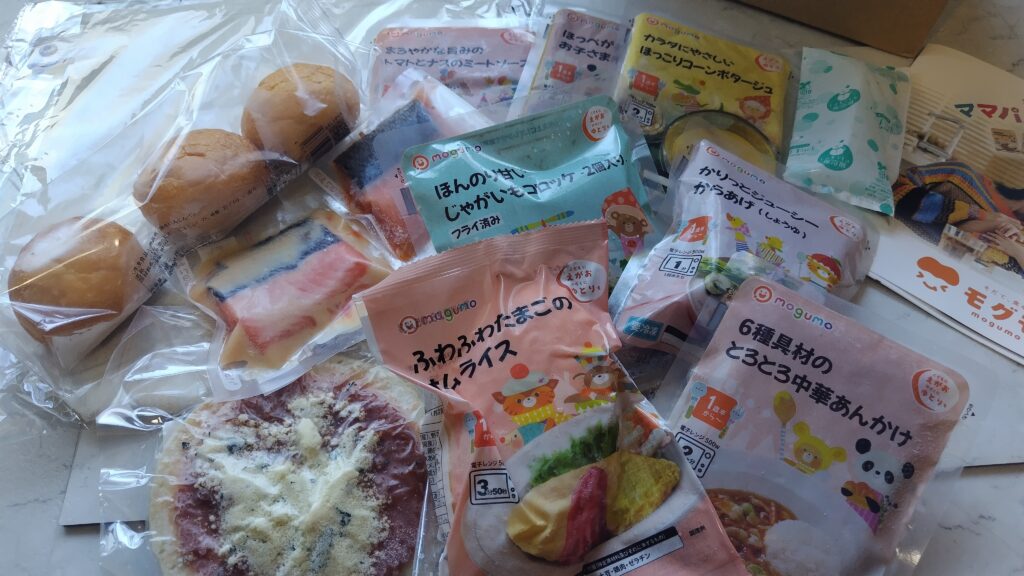 モグモの冷凍幼児食が届いたところ。ふわふわたまごのオムライスやとろとろ中華あんかけなど、複数のメニューのパッケージが並んでいる