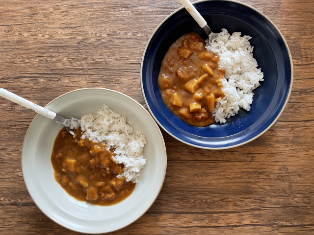 白い器と紺の器によそった子ども用のカレーライス。スプーンを添えて木のテーブルに置いたところ