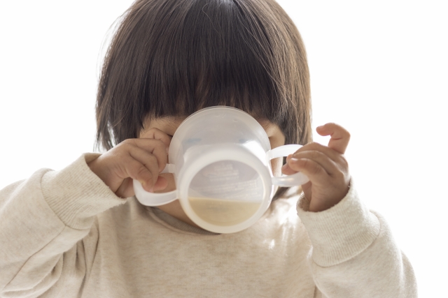 取っ手つきのコップを両手で持って自分で飲む子ども