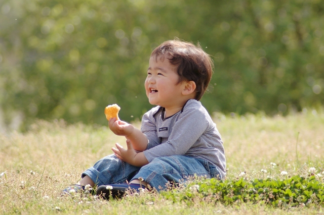 芝生に座って、おやつを手に持って笑っている子ども