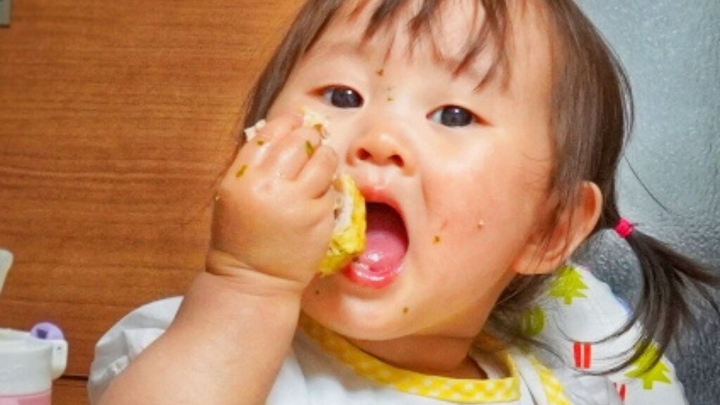 手に持った食べ物を、大きな口で頬張っている子ども