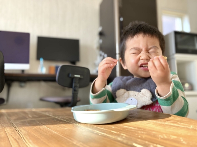 両手で食べ物を持って、目をぎゅっとつぶりながら前歯でかじっている子ども