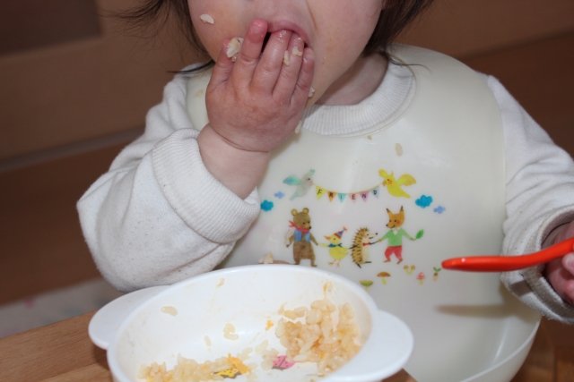 1歳の子が手づかみでごはんを食べ、そばにスプーンがある様子